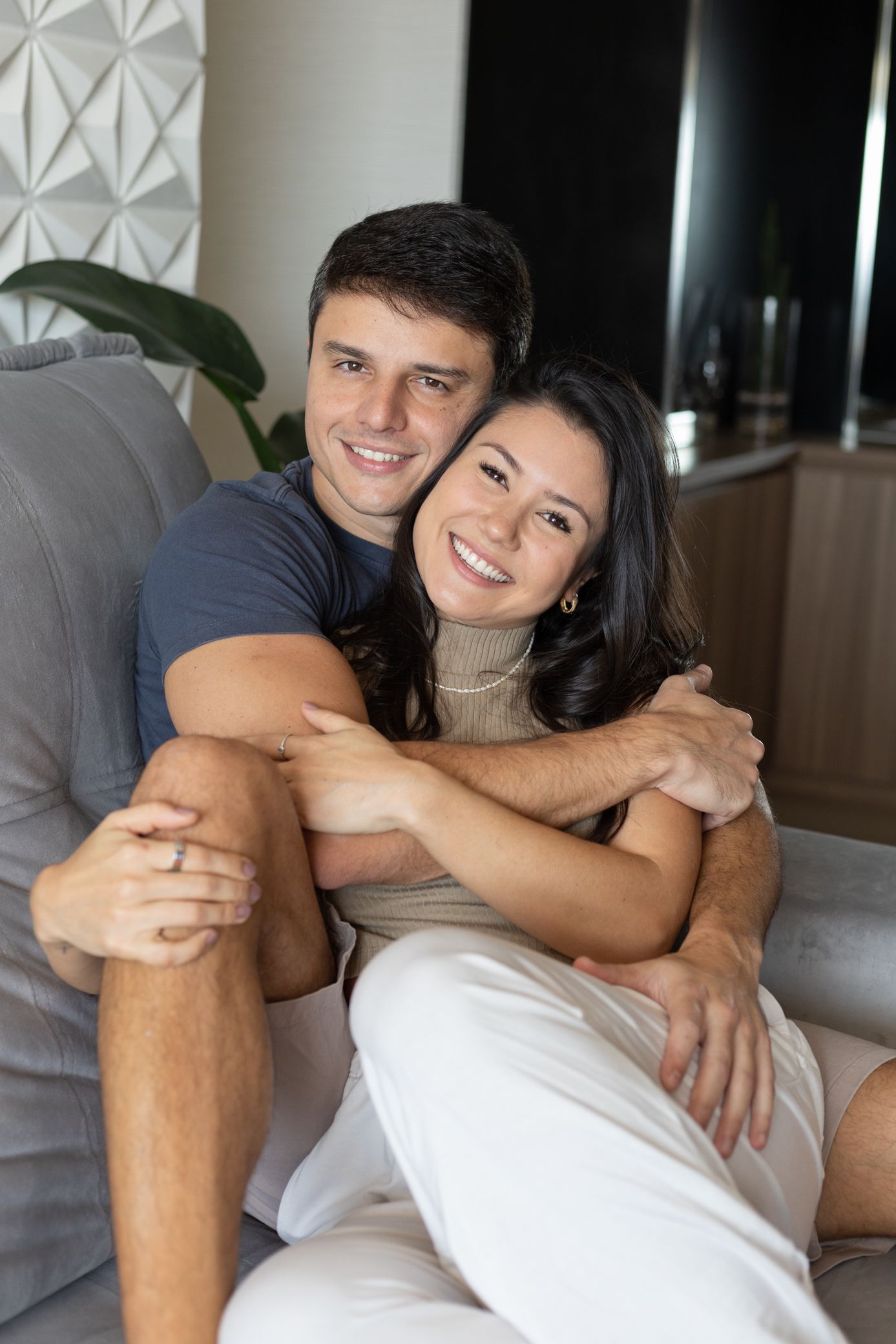 Happy couple embracing on a cozy sofa, smiling warmly in a modern living room setting.