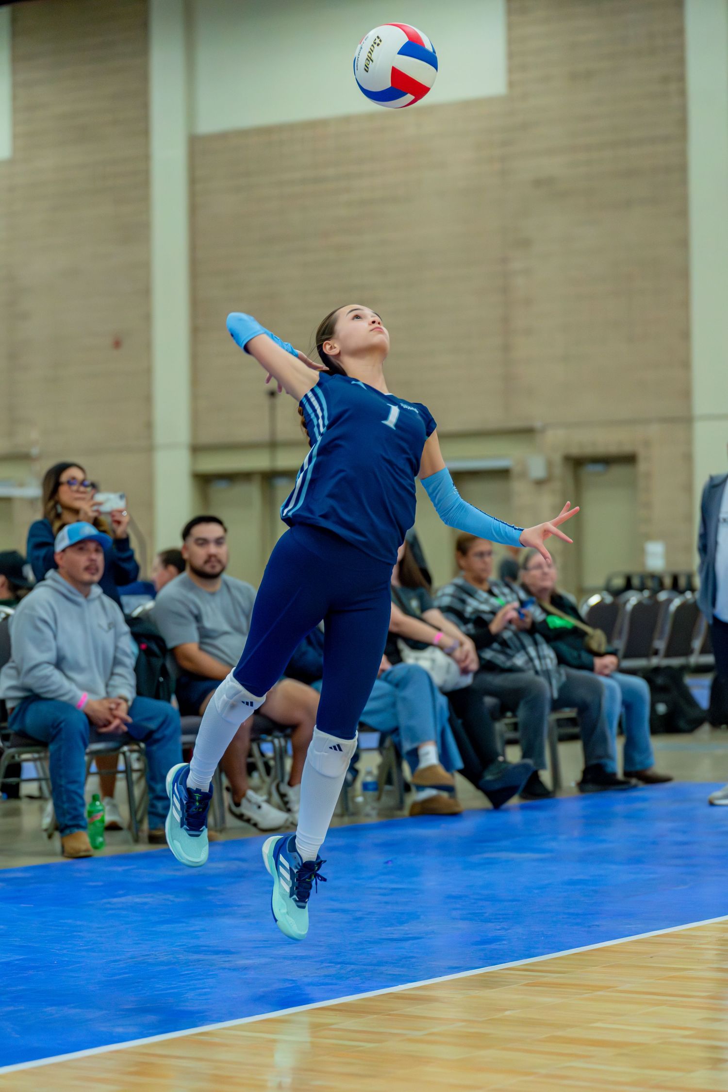 Volleyball player in navy blue uniform diving to save the ball during competitive indoor match.