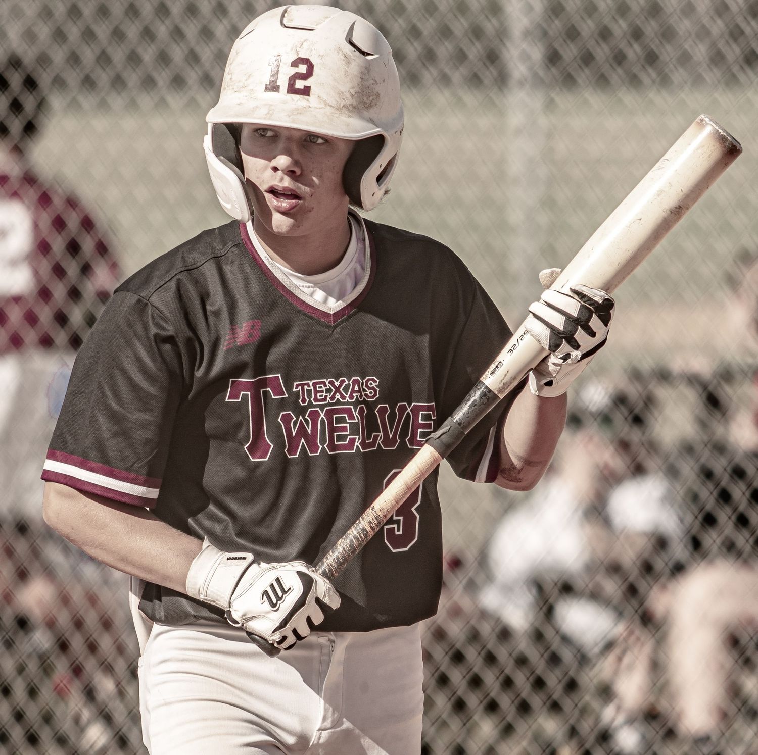 Baseball player in black jersey with number 12 helmet holds bat ready at plate.