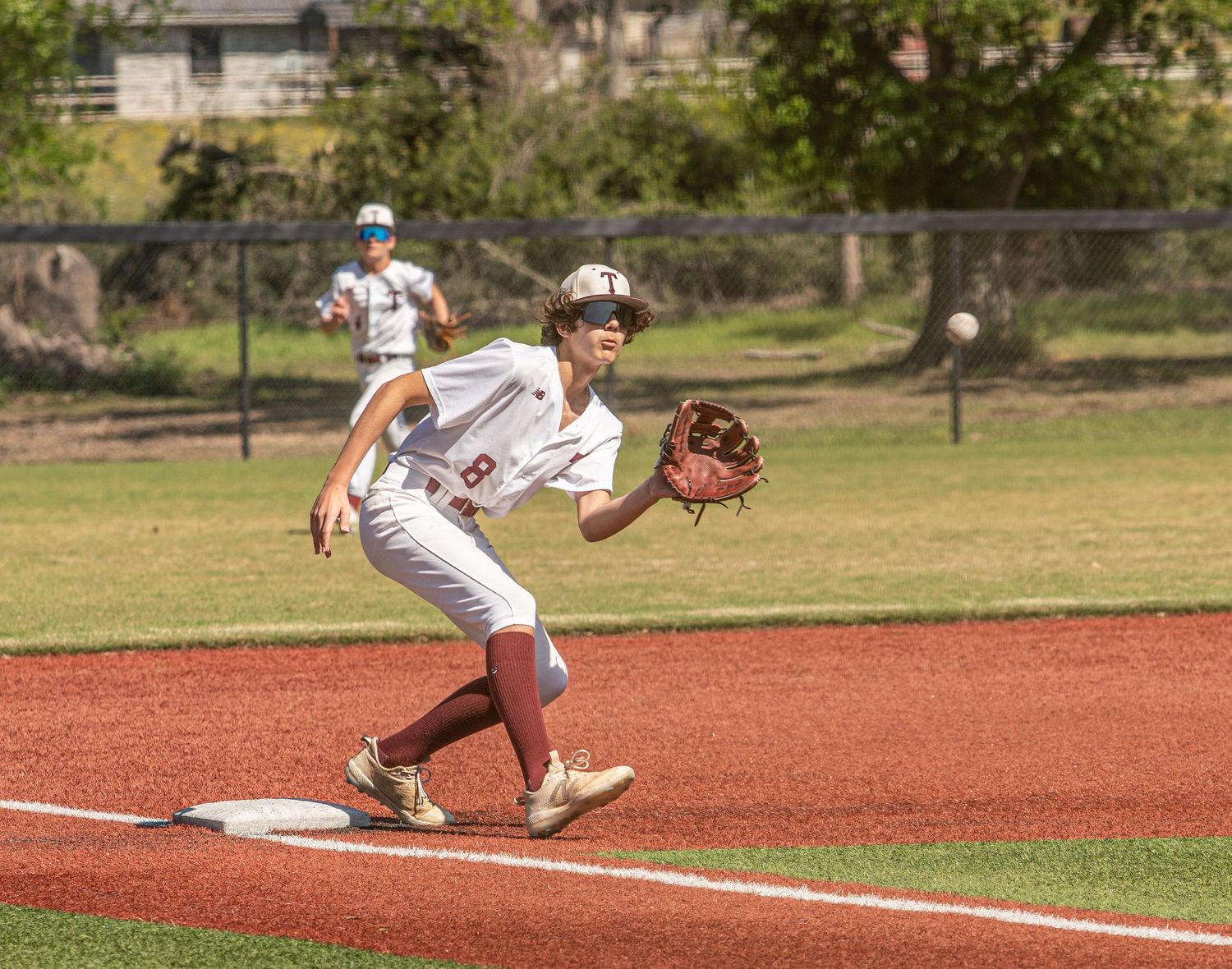 Baseball pitcher follows through on delivery motion on red clay mound during daytime game.