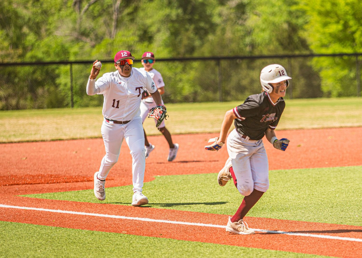 Baseball players in action during a play at first base on a sunny day.