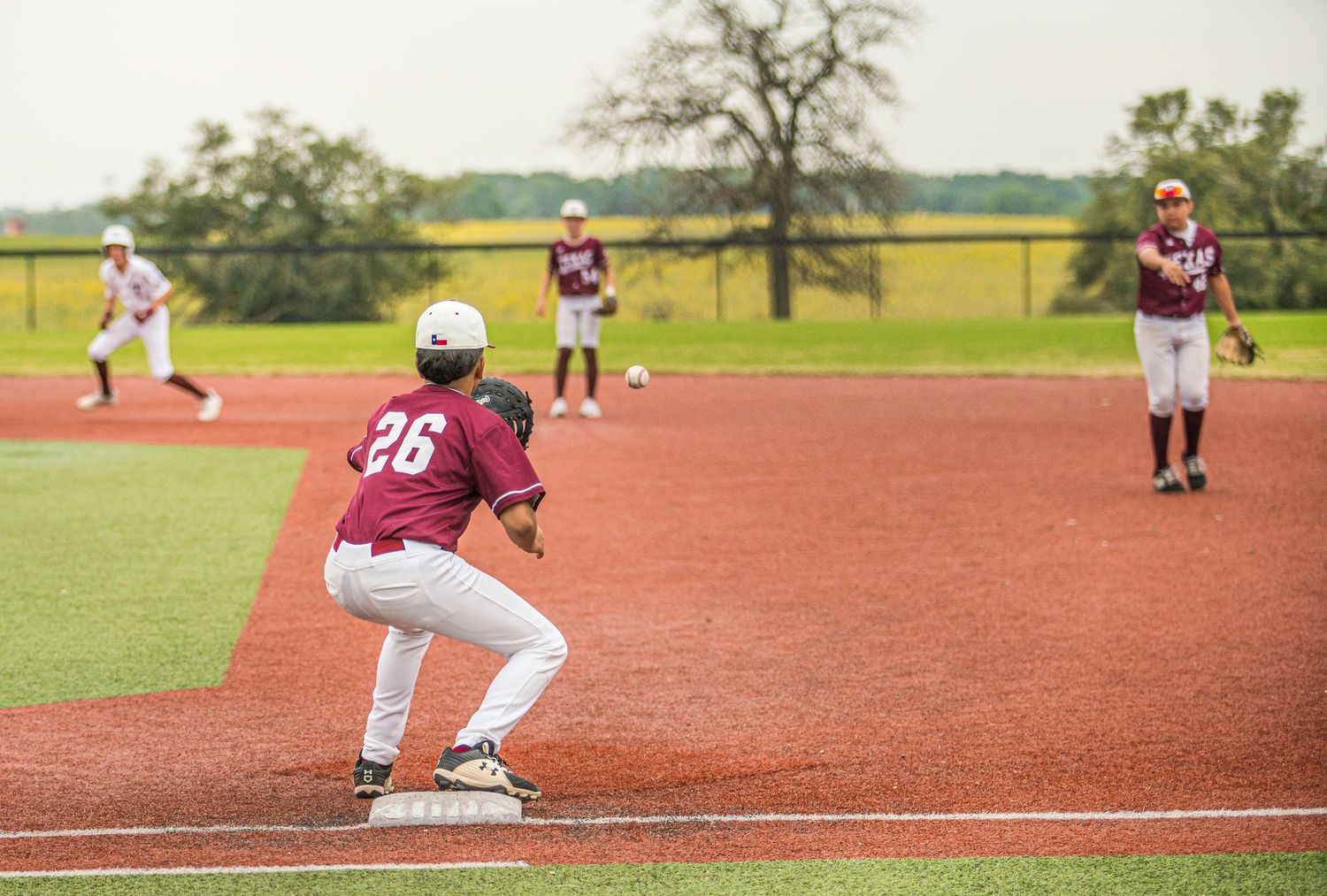 Baseball infielders in maroon and white uniforms positioned during game play.