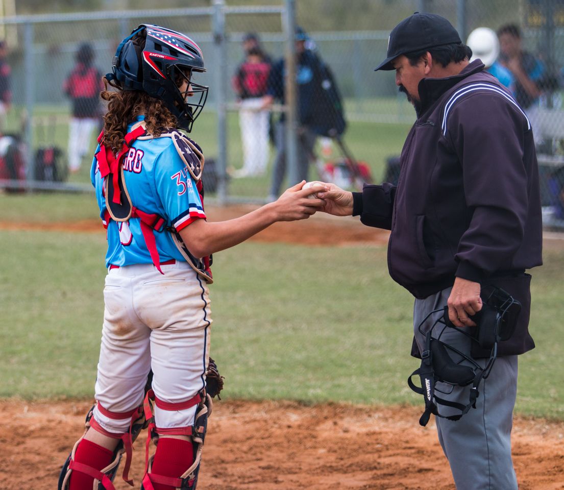 Baseball umpire and catcher discuss a call during a youth baseball game on a sunny afternoon.