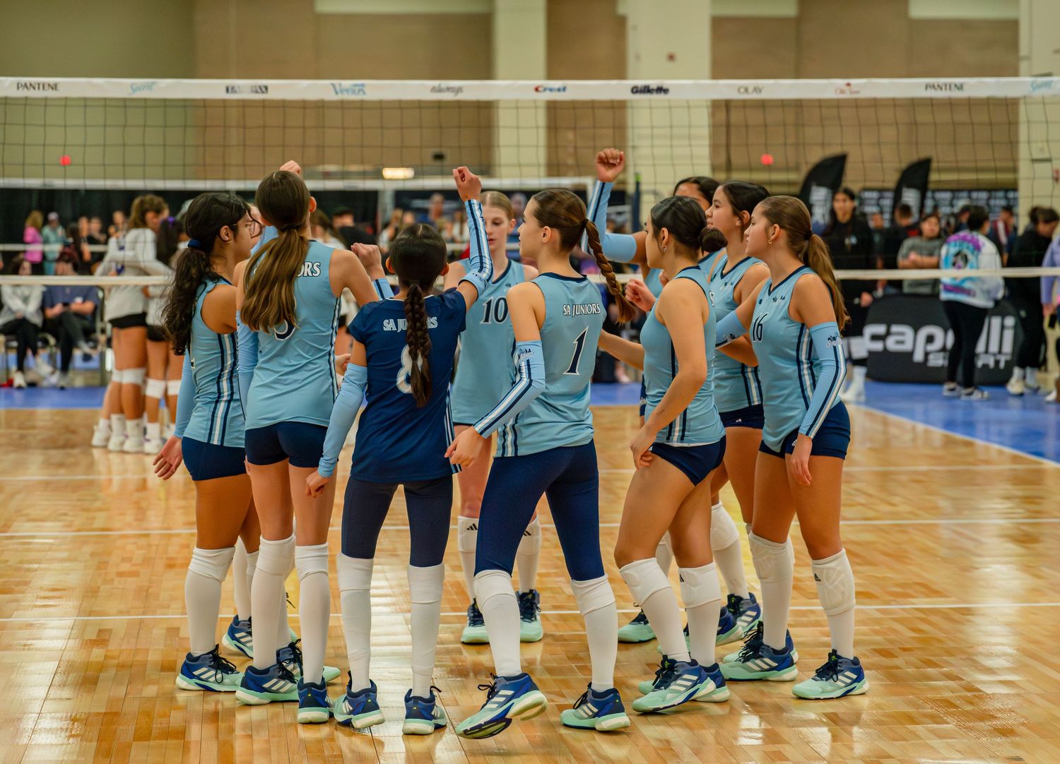 Teams in light blue uniforms gathered on volleyball court during tournament break.
