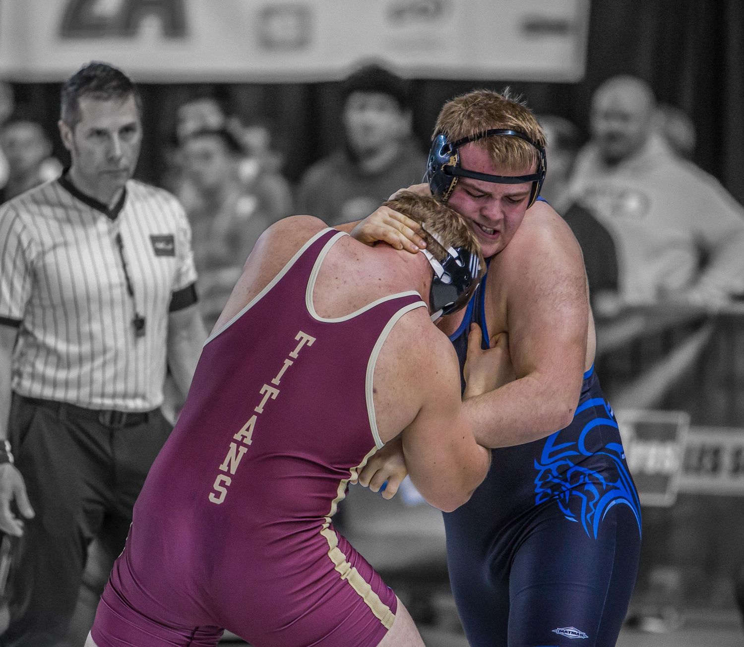 Two wrestlers compete in a close match wearing purple and blue uniforms on the mat.