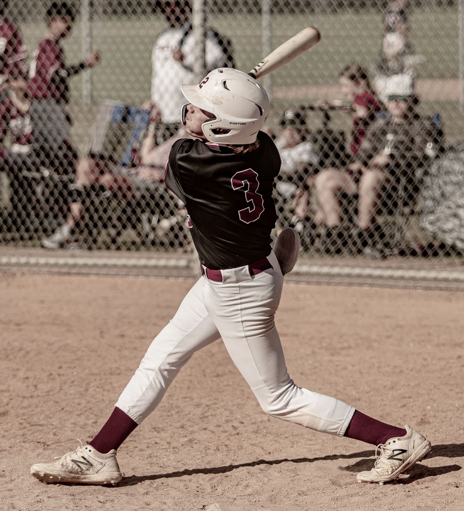 Baseball batter in black uniform swings bat during game with perfect follow-through form.