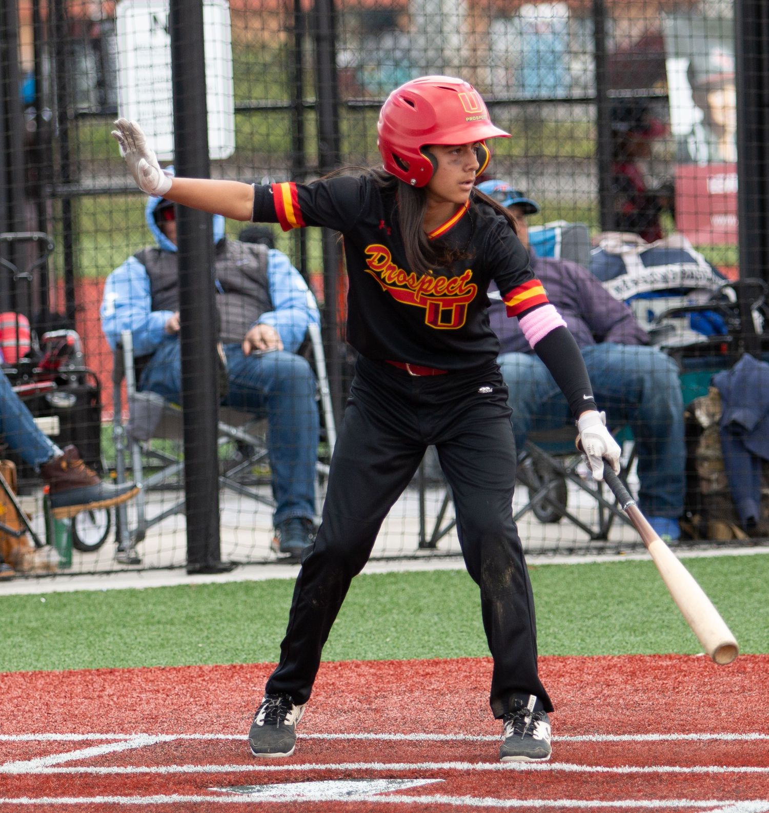 Baseball batter in black uniform and red helmet takes stance at home plate.
