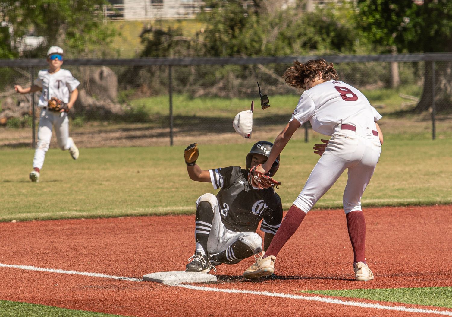 Baseball play at base shows fielder attempting to tag sliding runner during game action.
