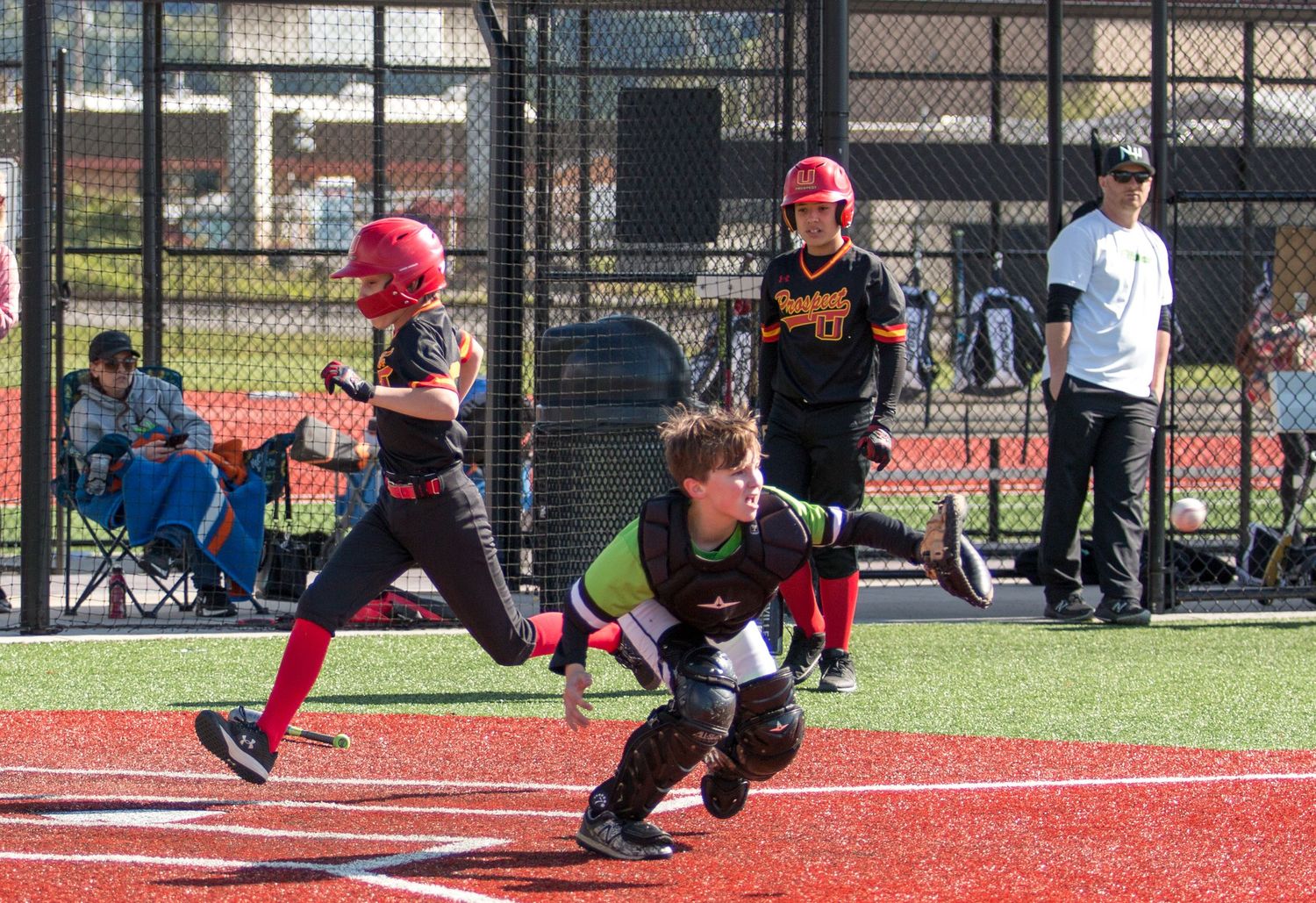 Baseball players slide into base during an intense game on a red turf field.