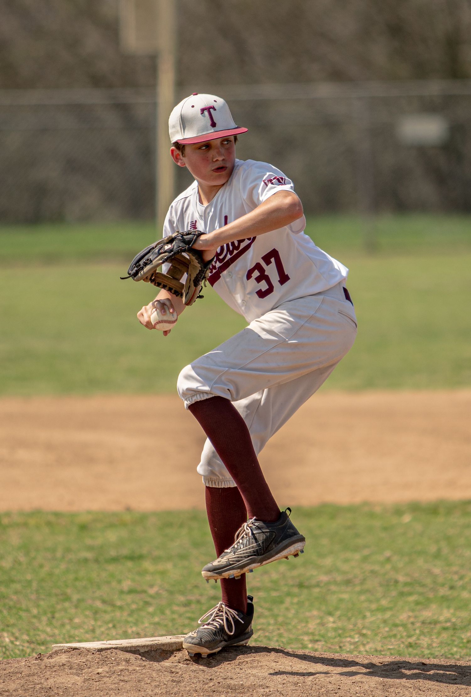 Baseball pitcher in white uniform number 37 winds up for a pitch on a dirt mound during a game.
