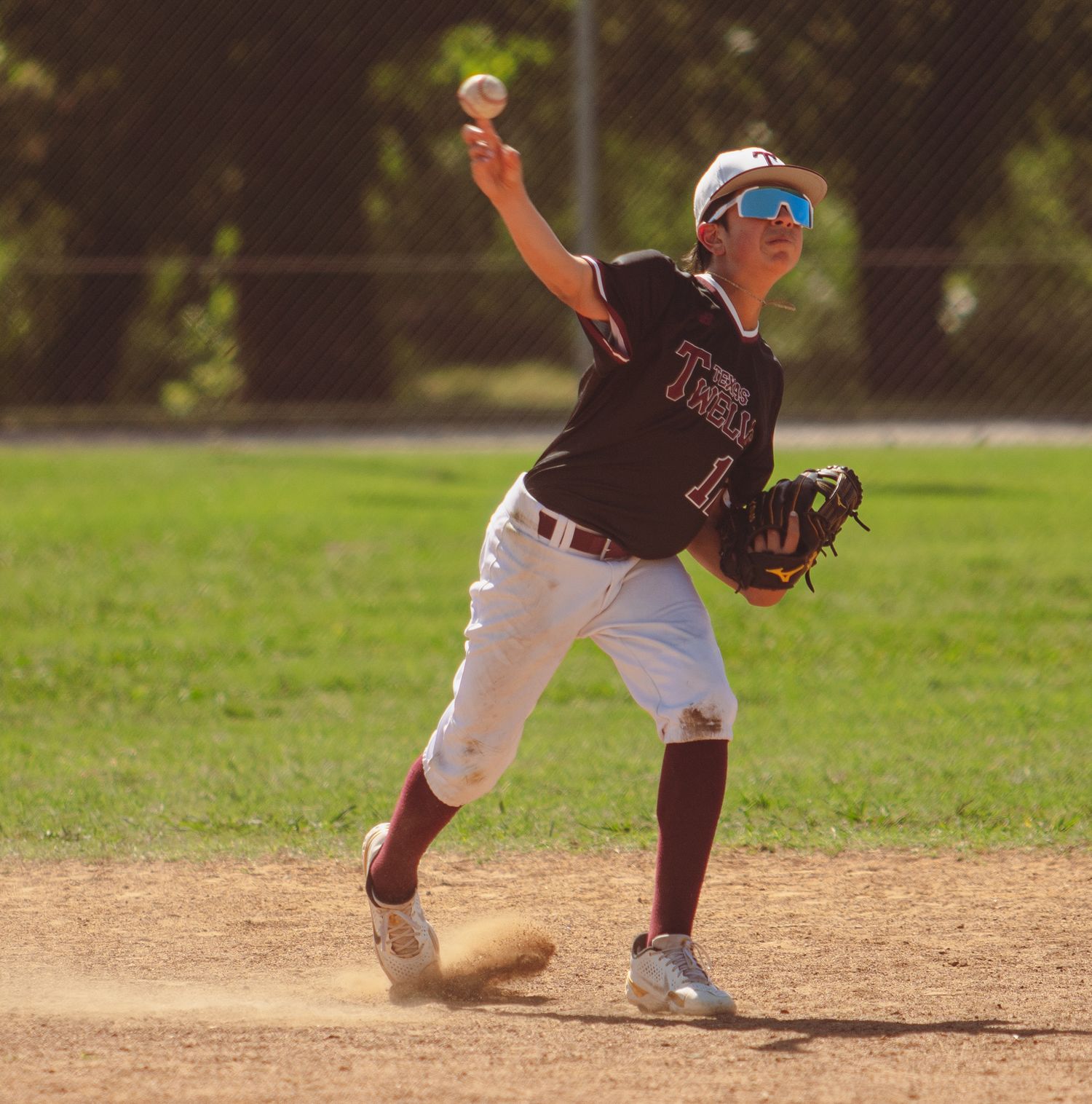 Baseball player in black uniform throws ball during game on sunny field.