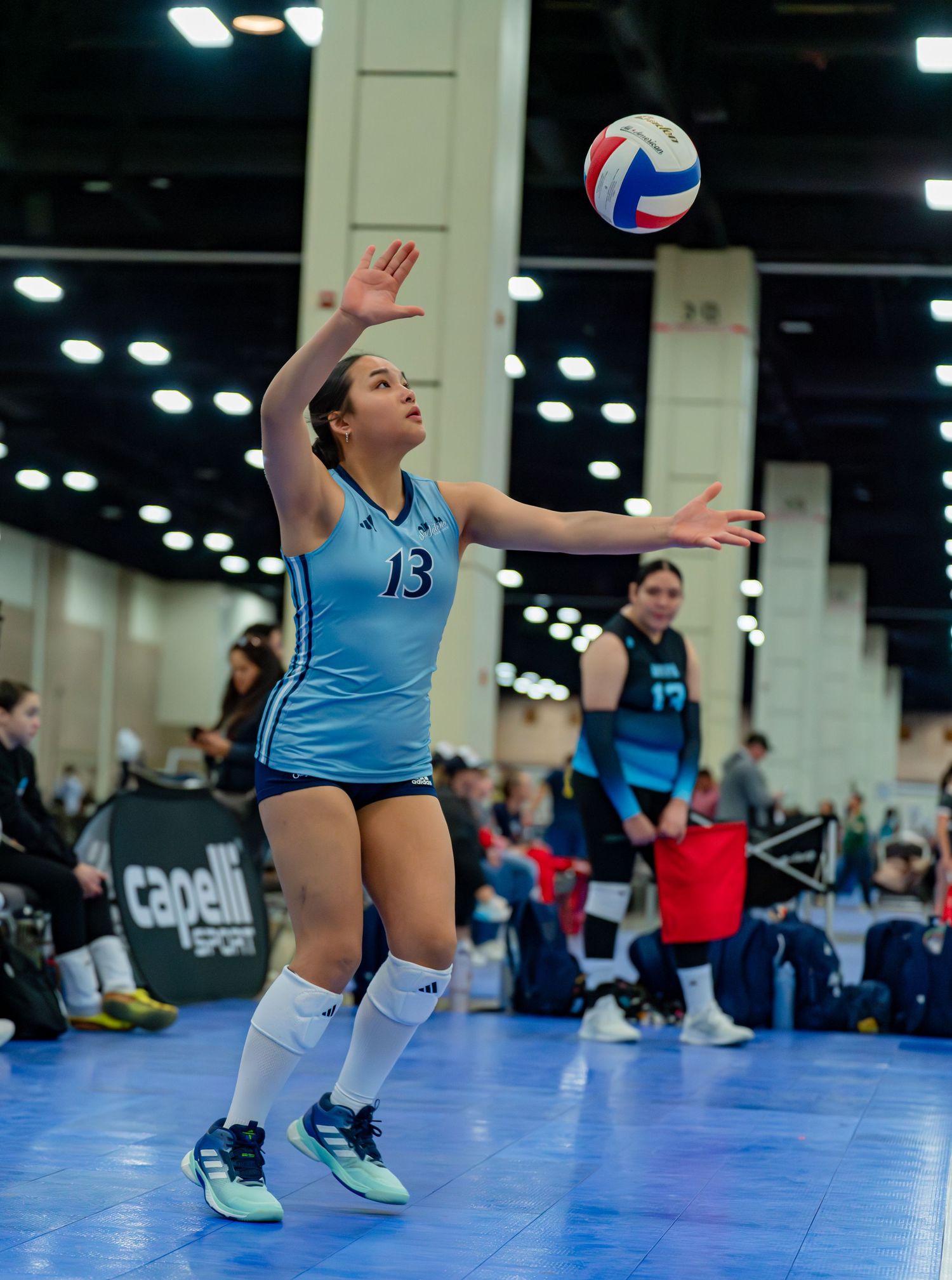 Volleyball player in light blue uniform diving for a ball during competitive match play.