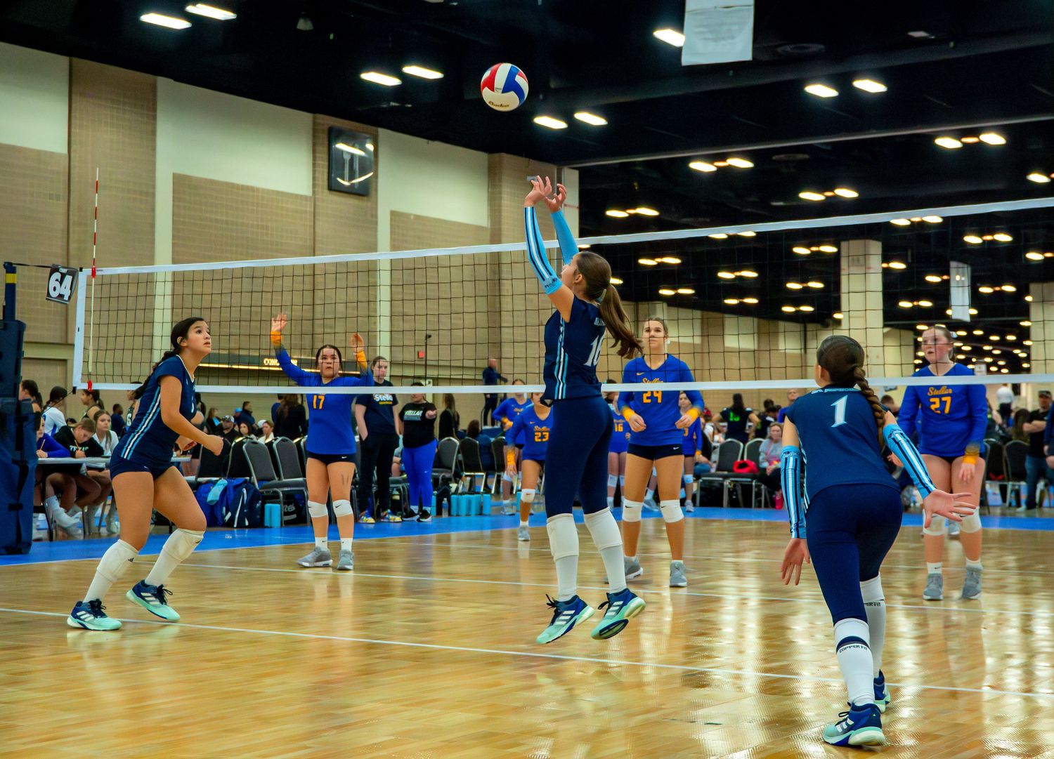 Panoramic shot of volleyball players in action on bright blue indoor court during tournament play.
