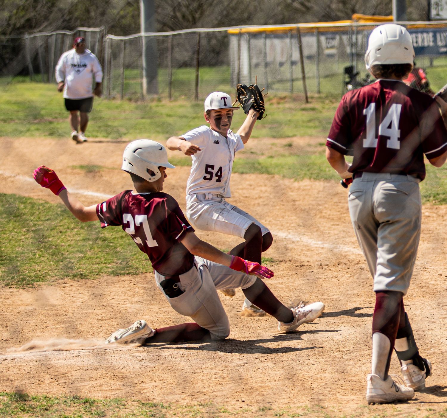 Baseball players compete at home plate with one sliding into base while others watch the play.