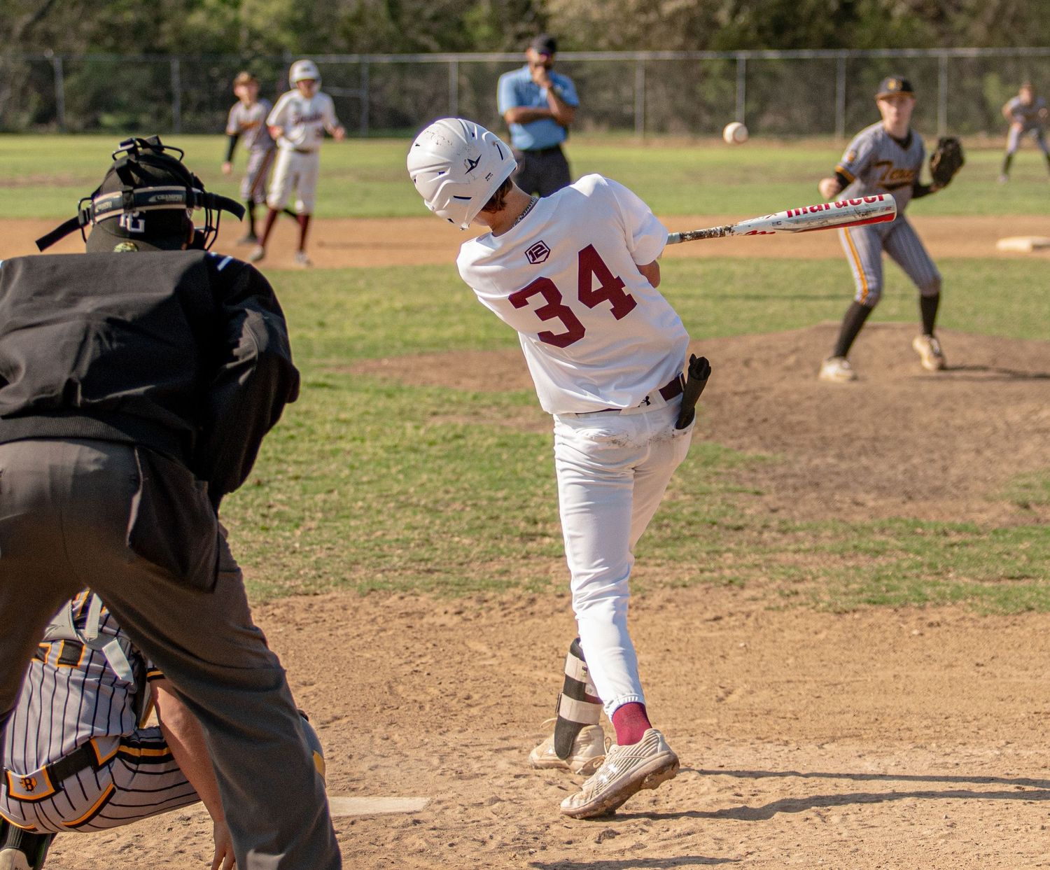 Baseball batter in white uniform number 34 swings at pitch while catcher and umpire watch from behind home plate.