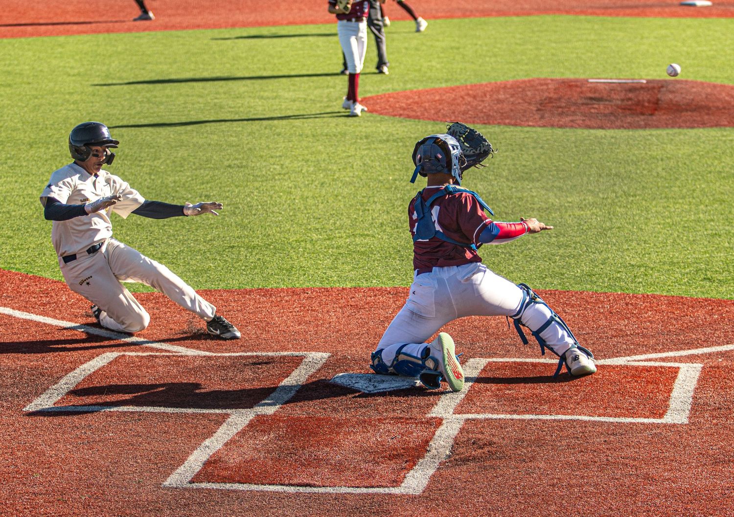 Baseball action at home plate shows sliding runner and catcher awaiting the throw.