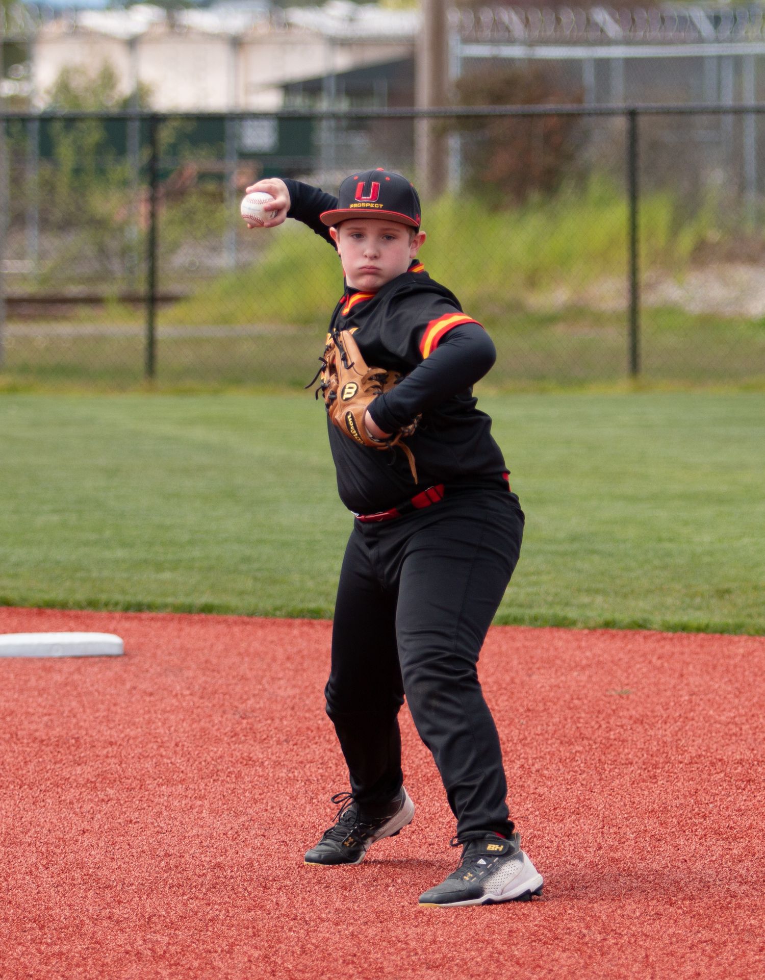 Youth baseball player in black uniform practicing fielding position on red infield dirt.