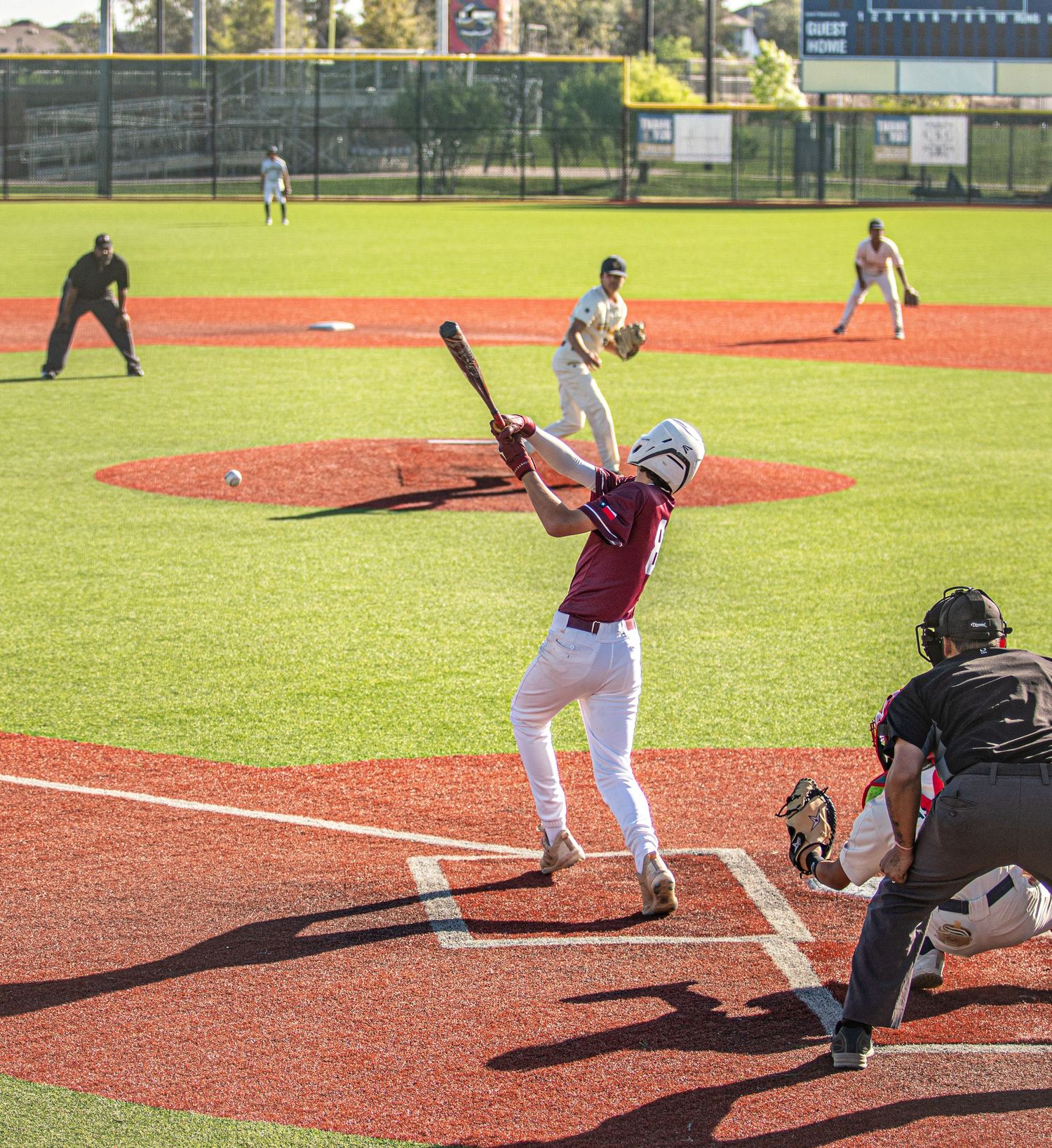 Baseball batter in maroon uniform takes a powerful swing at home plate during a game.