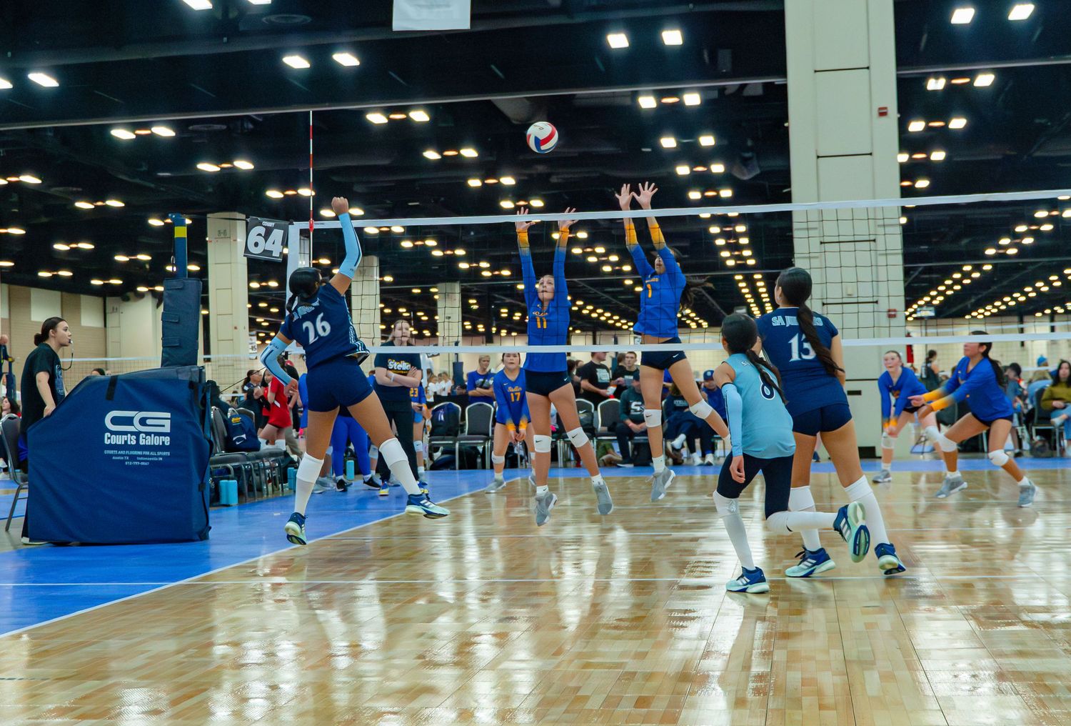 Panoramic shot of volleyball courts with teams practicing and competing in a spacious indoor facility.