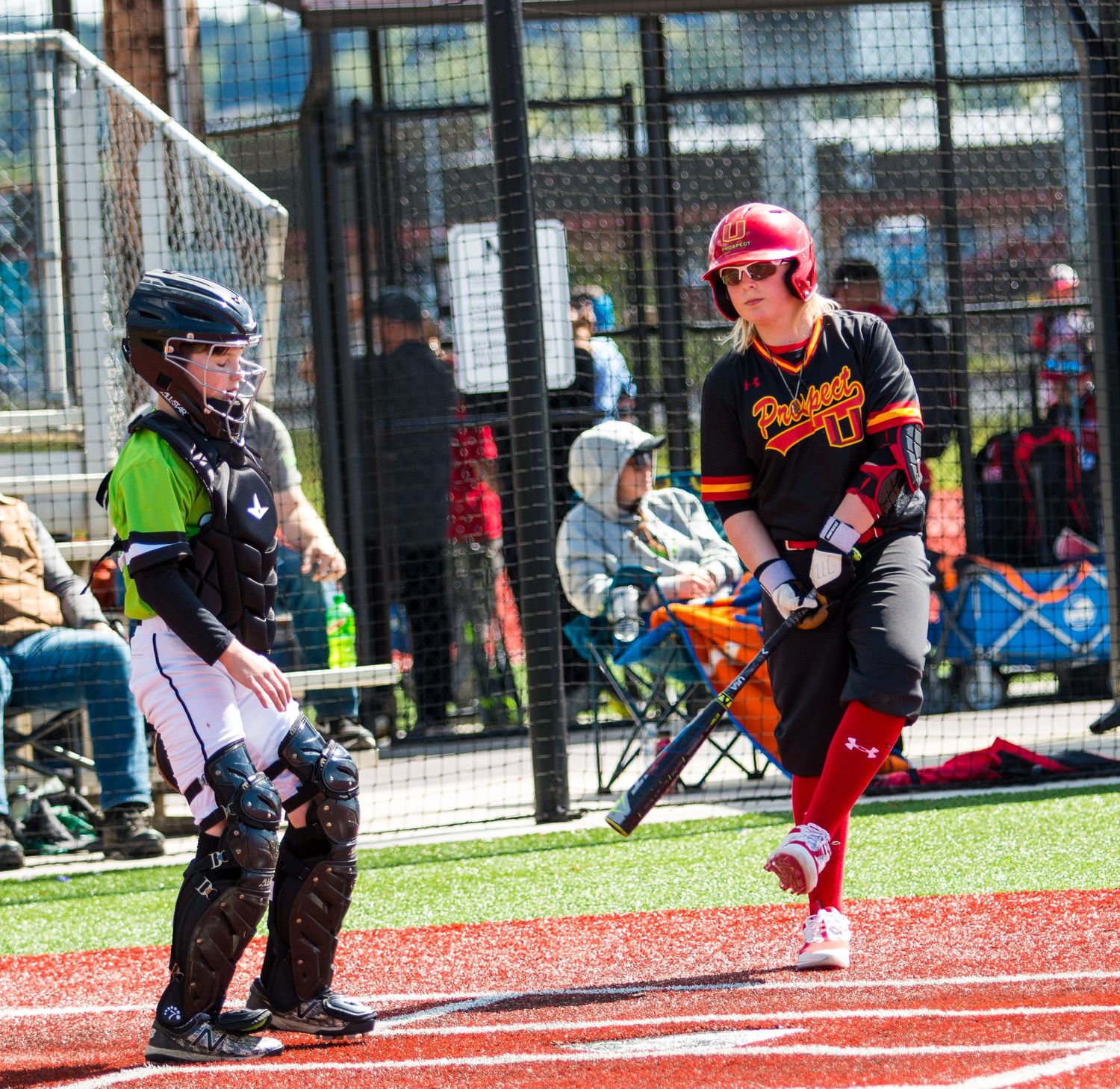 Baseball player in black and red uniform runs past home plate during game.