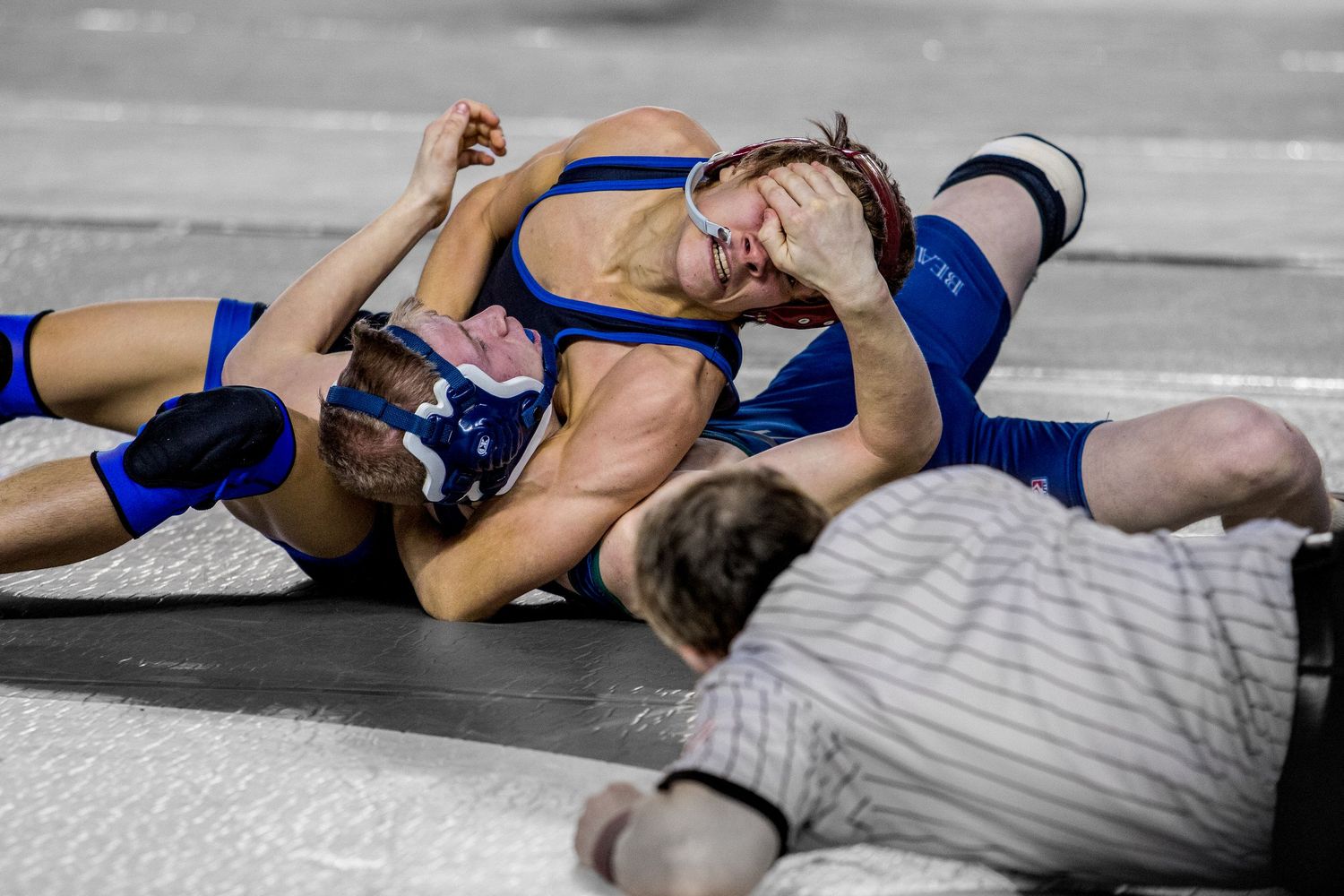 Wrestling match sequence showing athletes in blue uniforms competing on the mat.