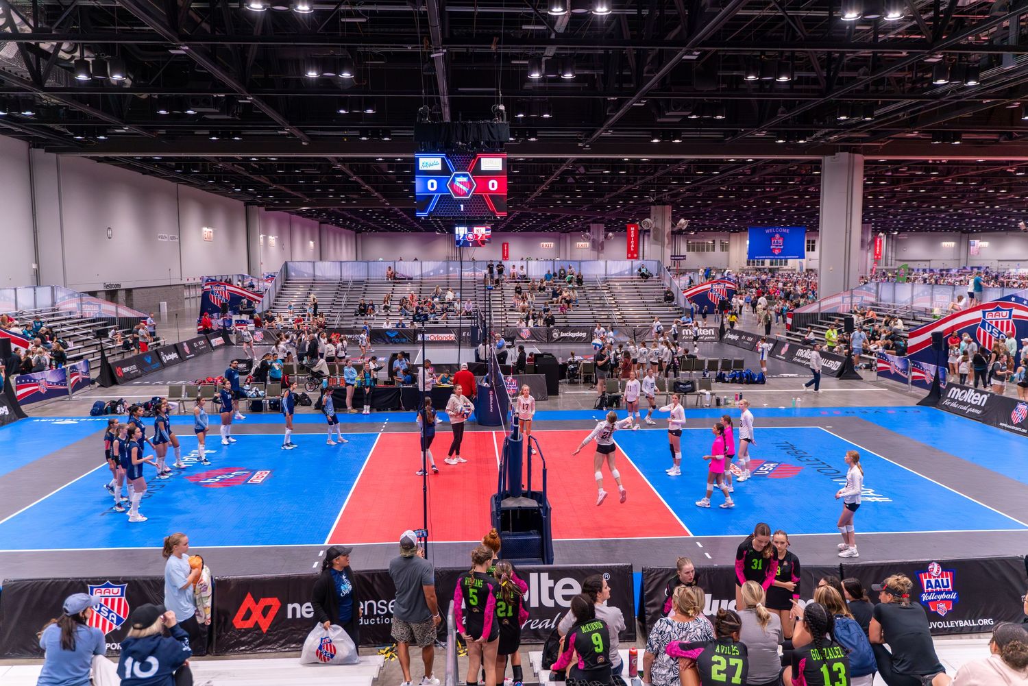 Aerial view of multiple volleyball courts during large indoor tournament.