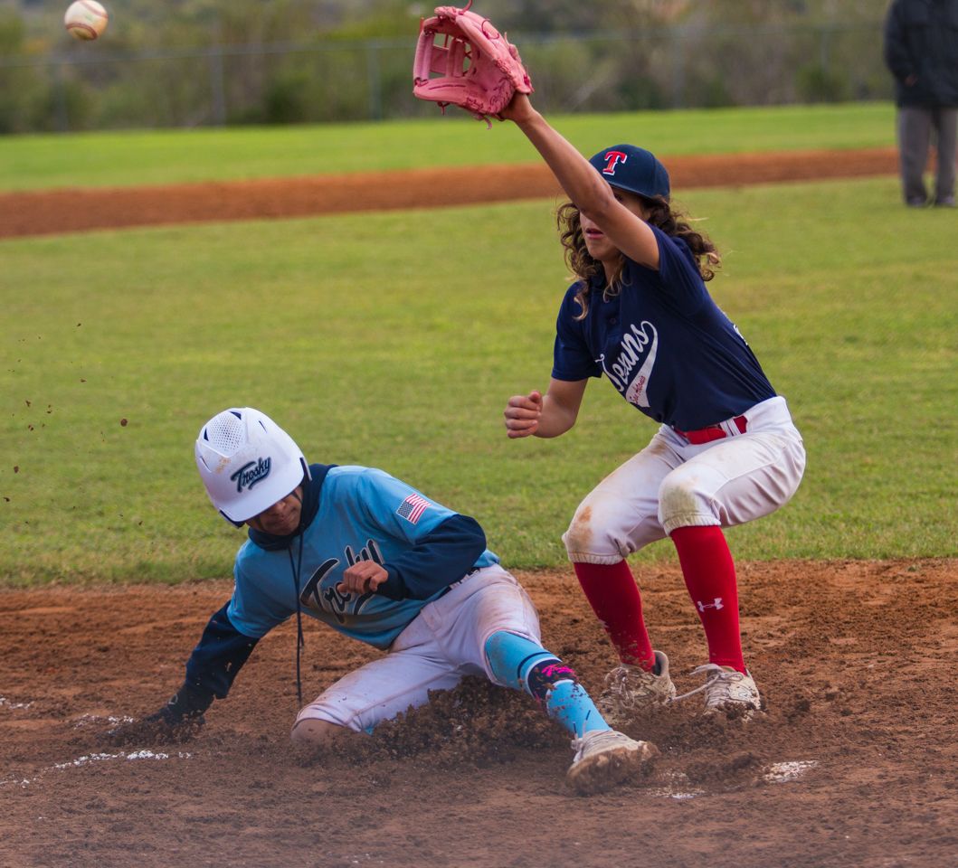 Baseball player slides into base during game as infielder reaches to make the tag on the dusty field.