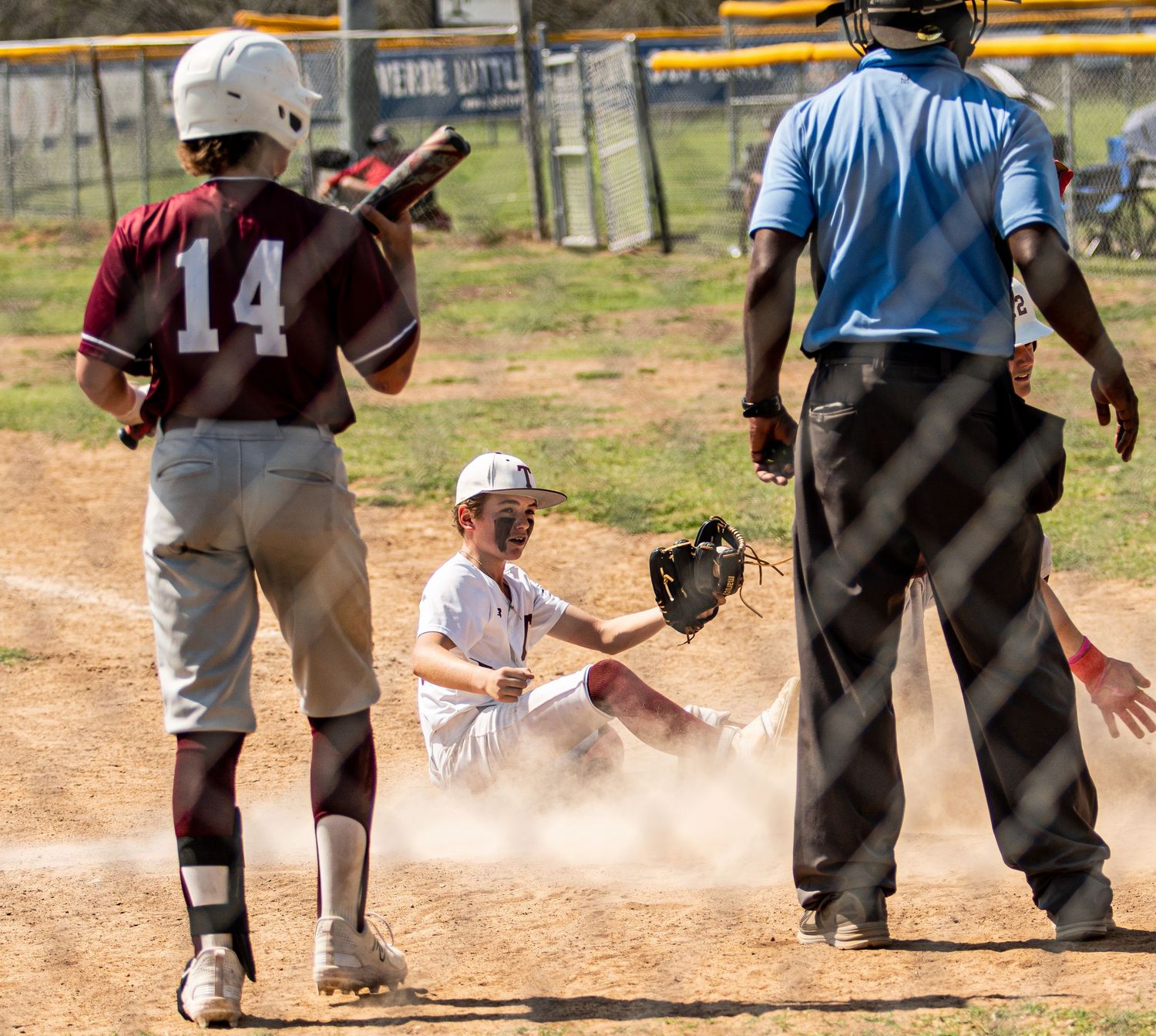 Baseball play at home plate creates dust cloud as players and umpire observe the action.