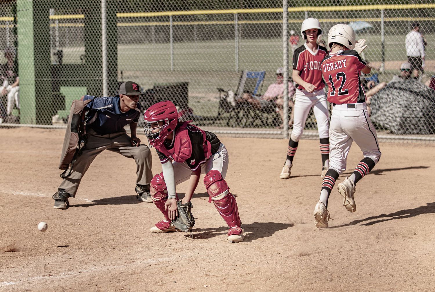 Baseball action shot showing catcher fielding ball as runner approaches home plate during game play.
