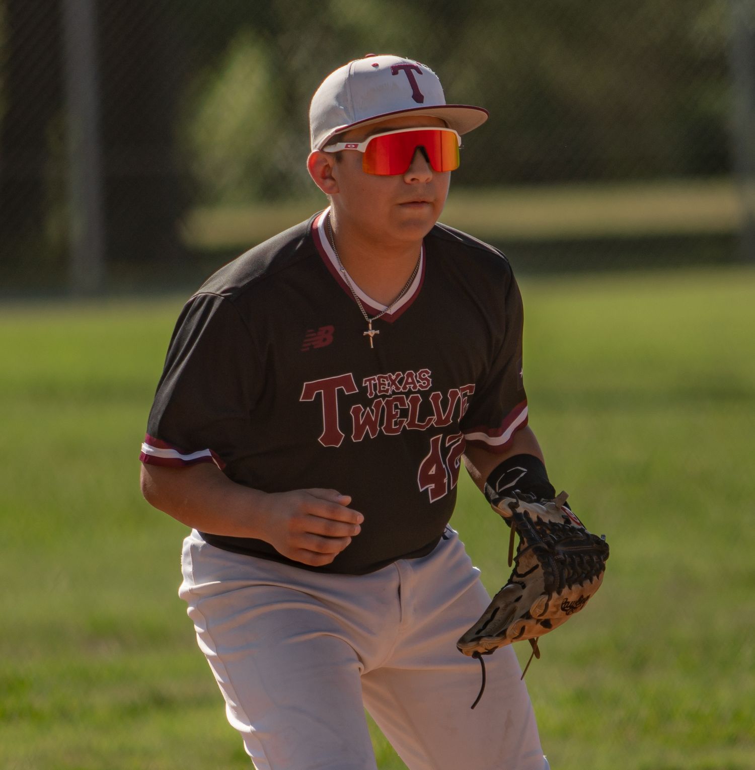 Youth baseball players in white and maroon uniforms fielding on a sunny day.