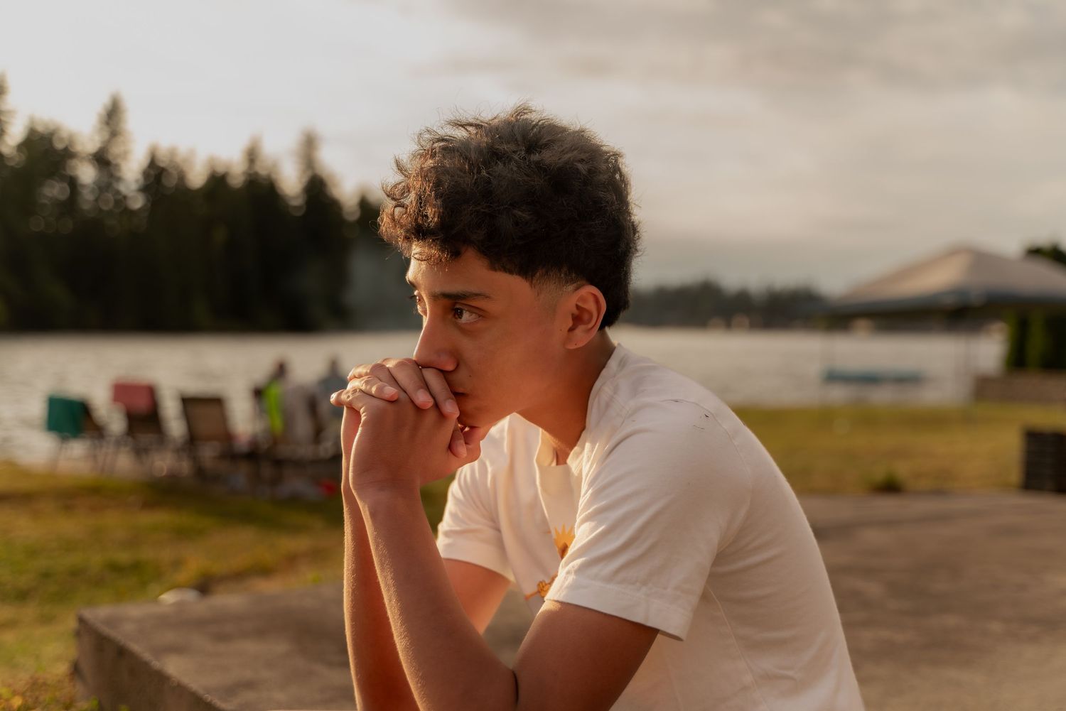 Person in white shirt sitting outdoors during golden hour with trees in background.