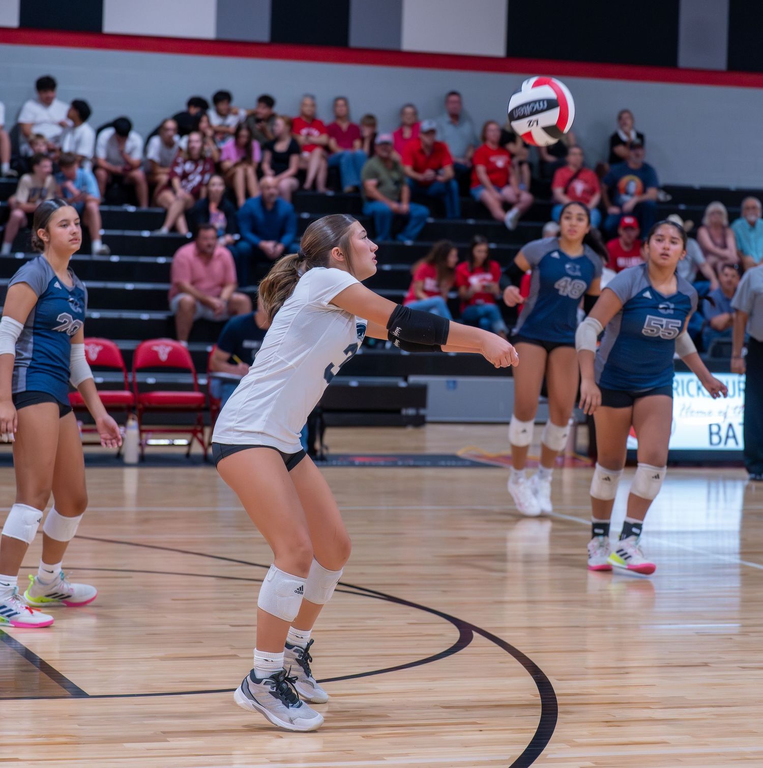 Indoor volleyball players diving and reaching for the ball during competitive match play.