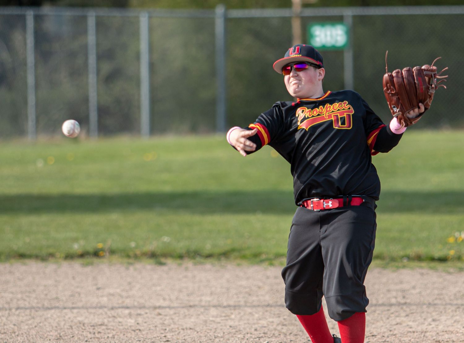 Baseball player in black and red uniform making a diving catch attempt on the field.