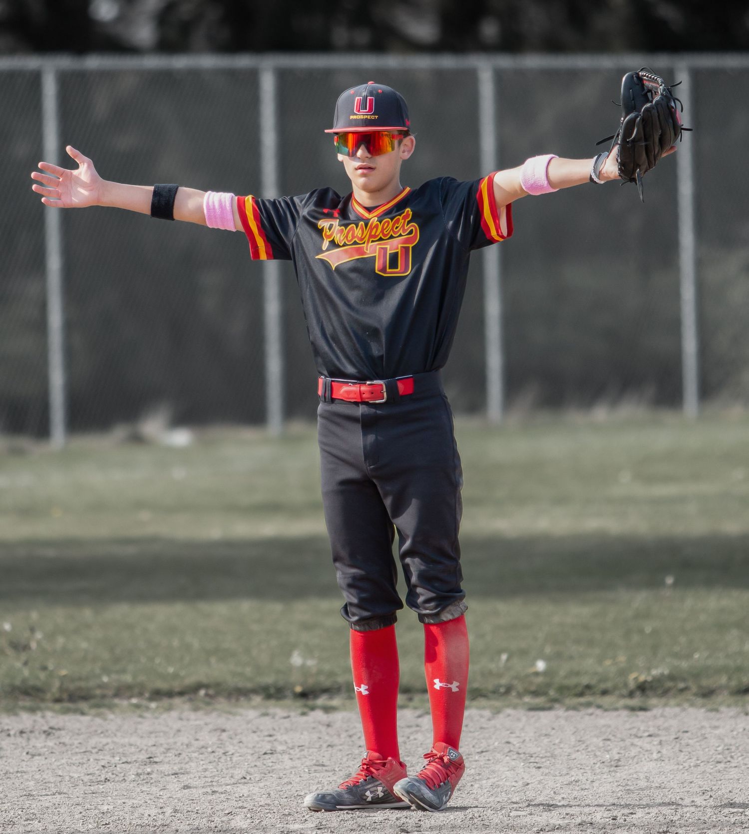 Young baseball player in black uniform and red socks demonstrates fielding positions on dirt infield.