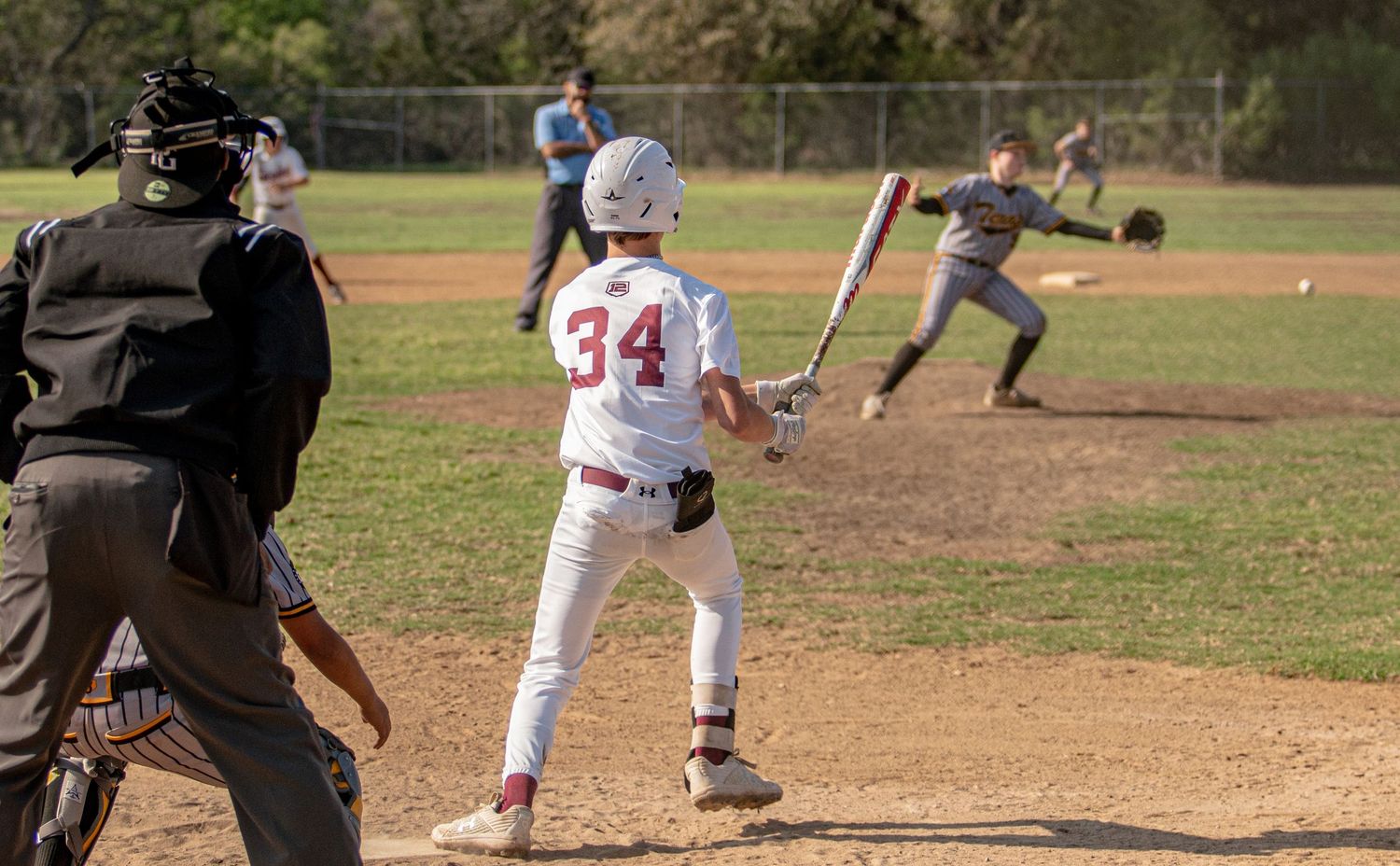Baseball player in white uniform at bat while catcher and umpire observe the play.