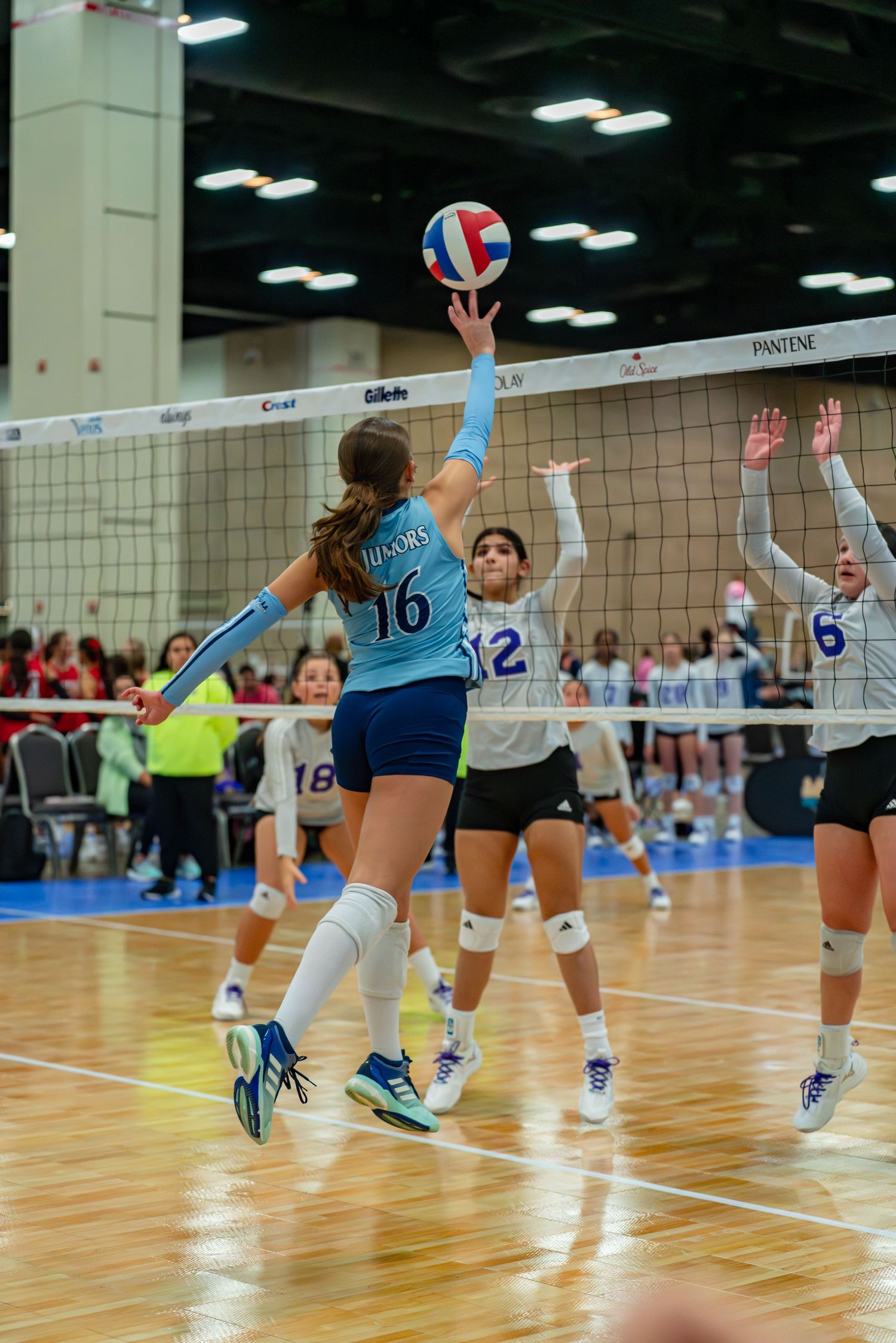 Action shot of volleyball players jumping at the net during an indoor match on wooden courts.