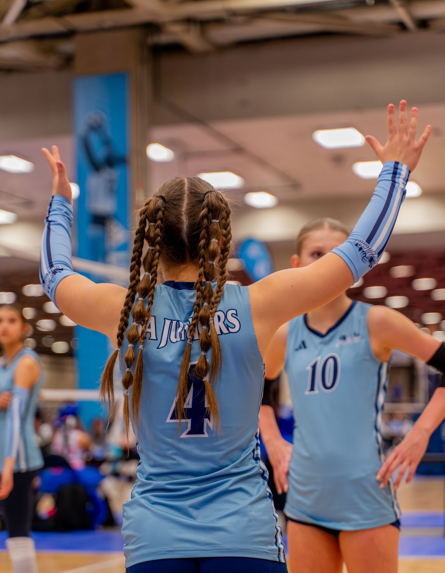 Players in light blue jerseys celebrate during a volleyball match with raised hands and high fives.