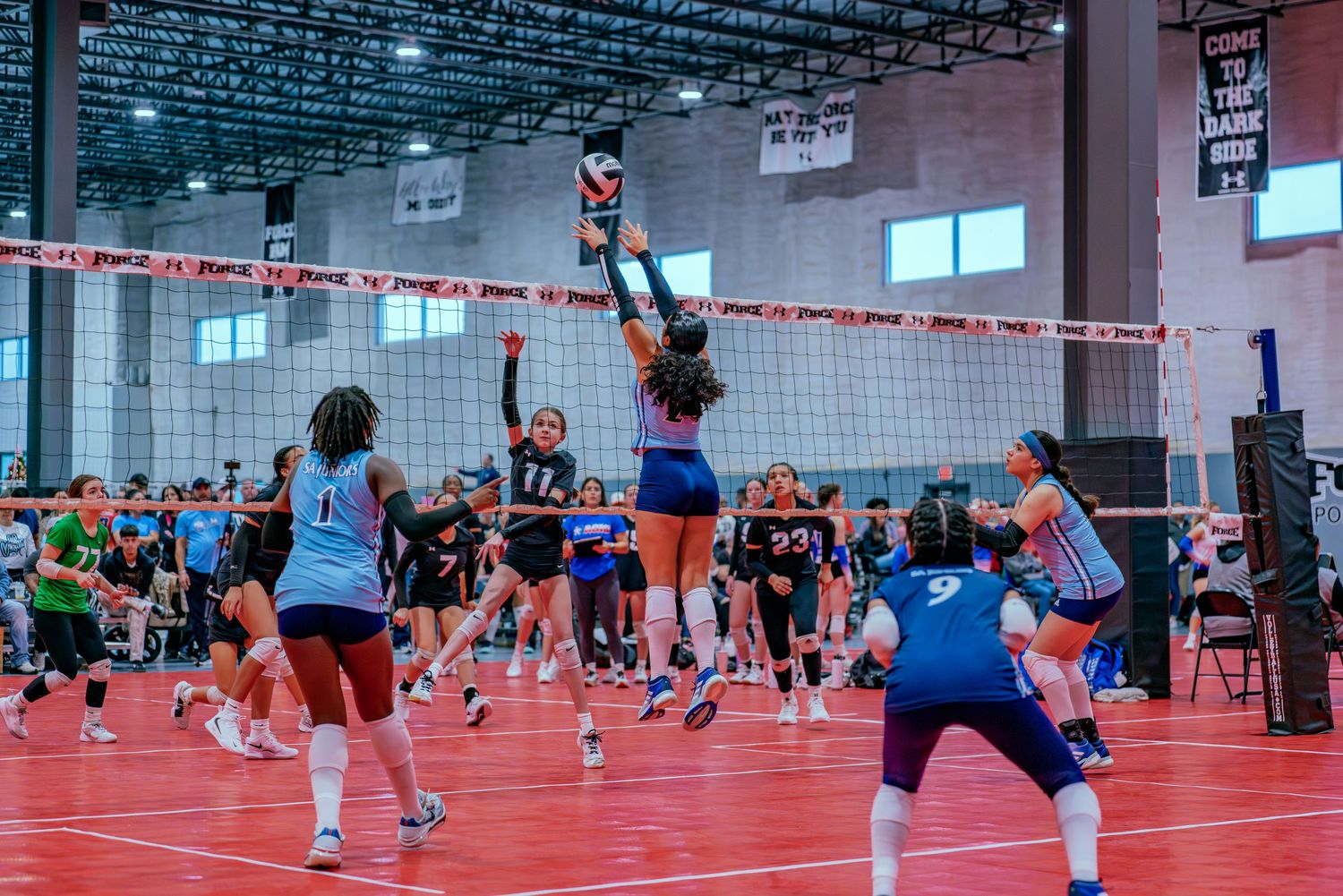 Players jump for block attempt during competitive volleyball match.