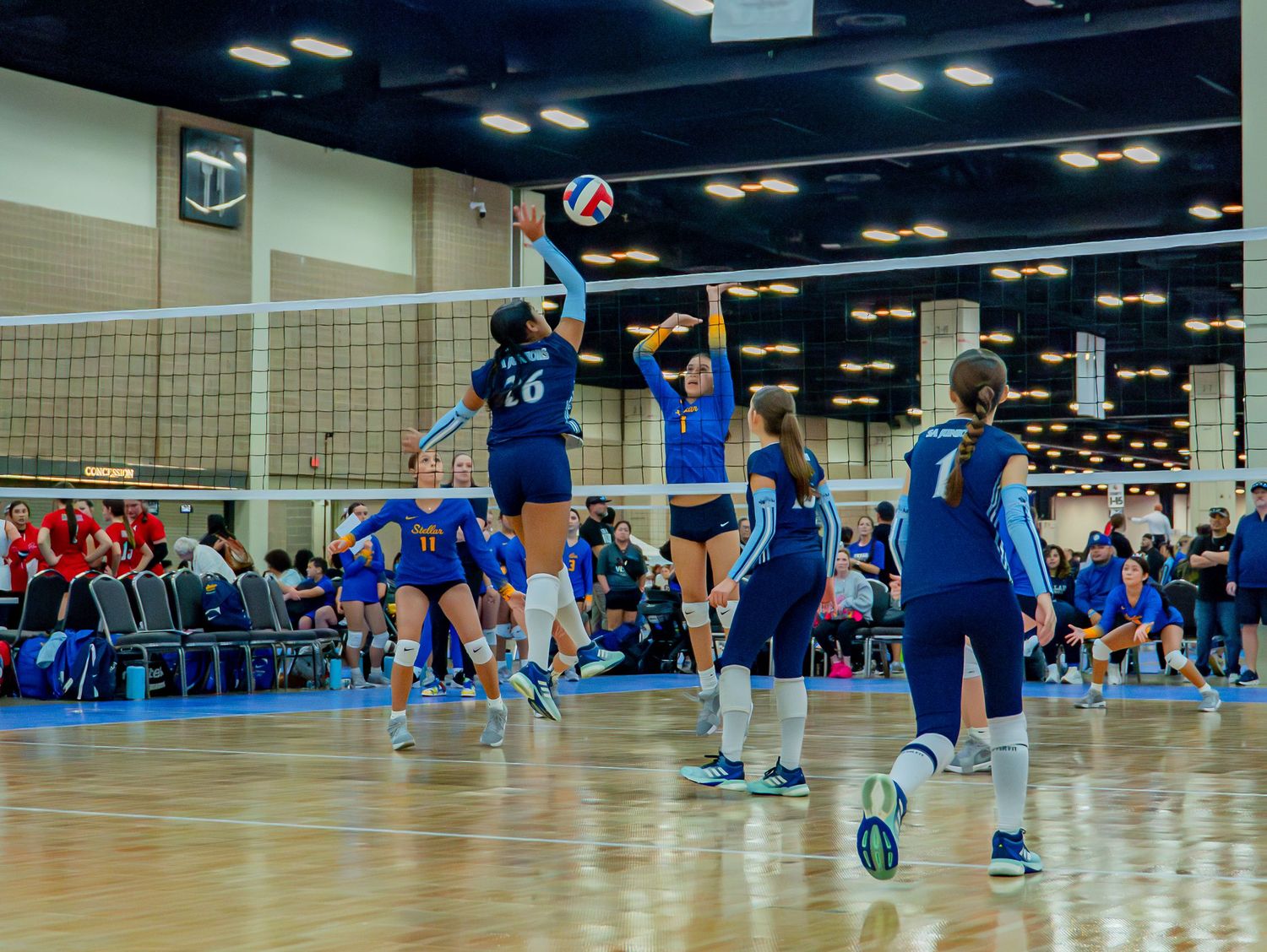 Indoor volleyball tournament with multiple courts showing players in action.