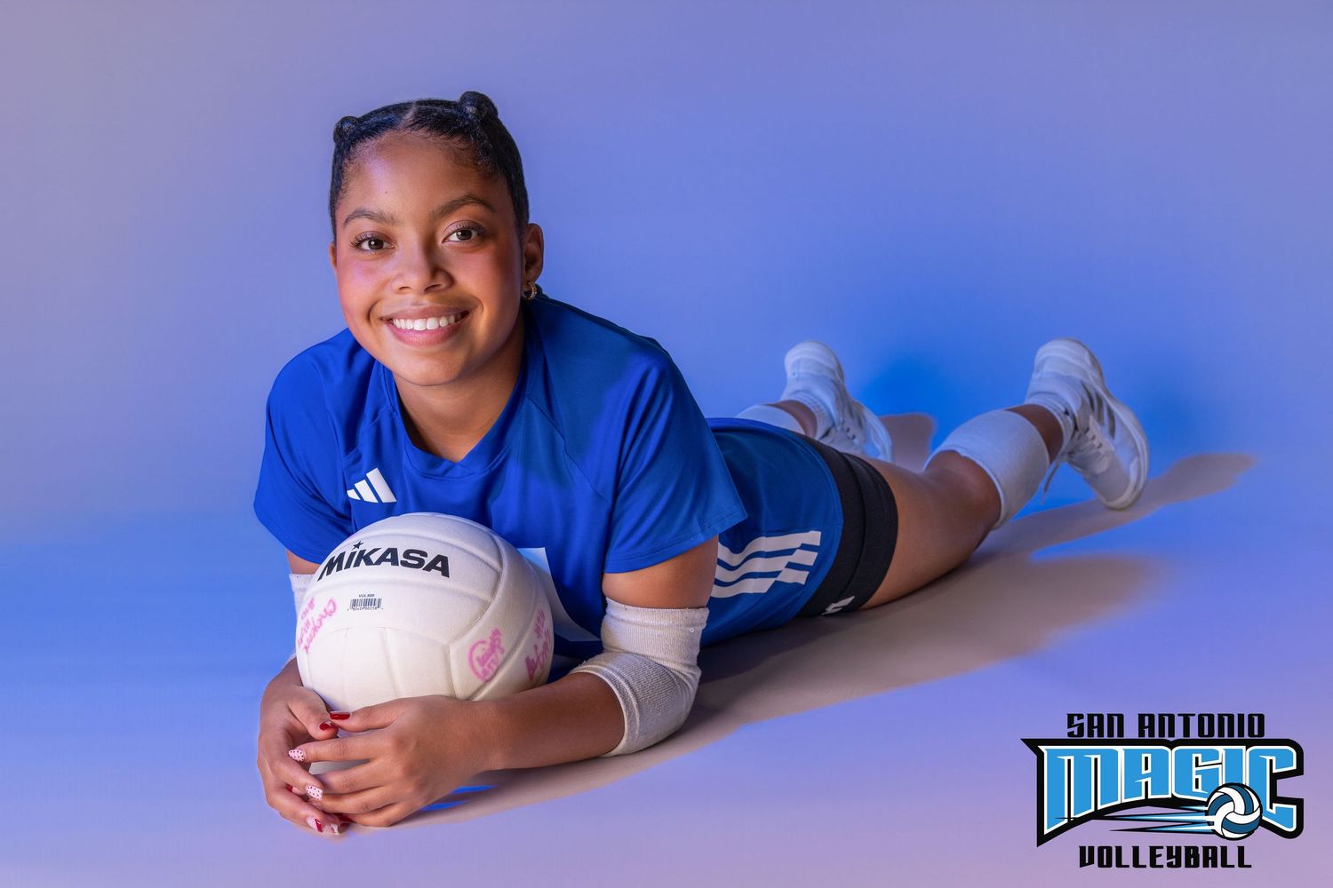 Player poses with volleyball in blue uniform against gradient studio lighting.