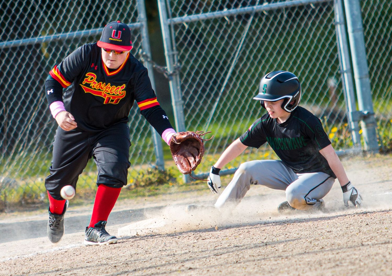 Baseball player sliding into base while opponent attempts to make the tag during game play.