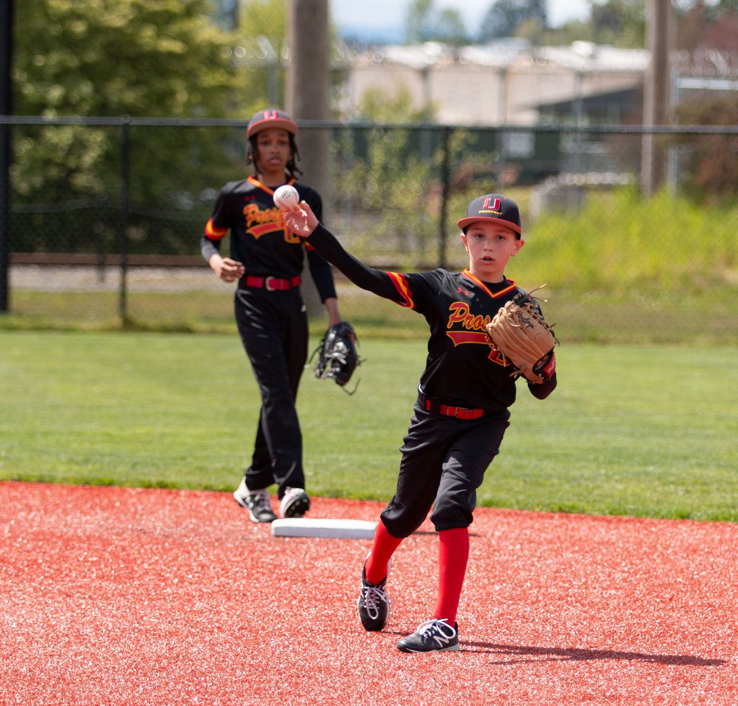Baseball players in black uniforms make defensive play on red turf infield.