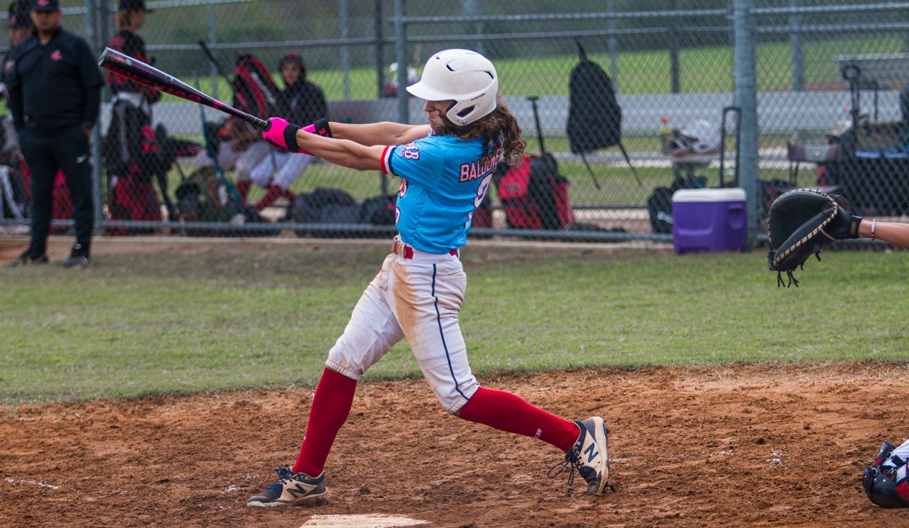 A baseball player in a red uniform slides into base during a competitive game on a dirt infield.