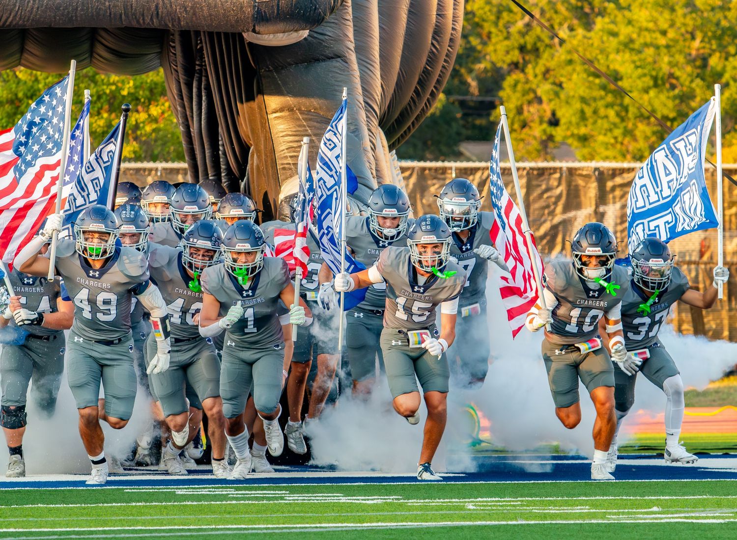 Football team running onto field with American flags and smoke effects.
