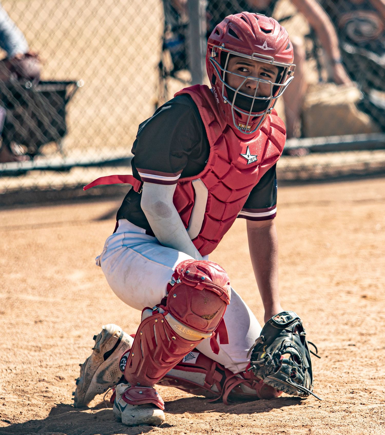 Baseball catcher in red gear crouches in ready position behind home plate.