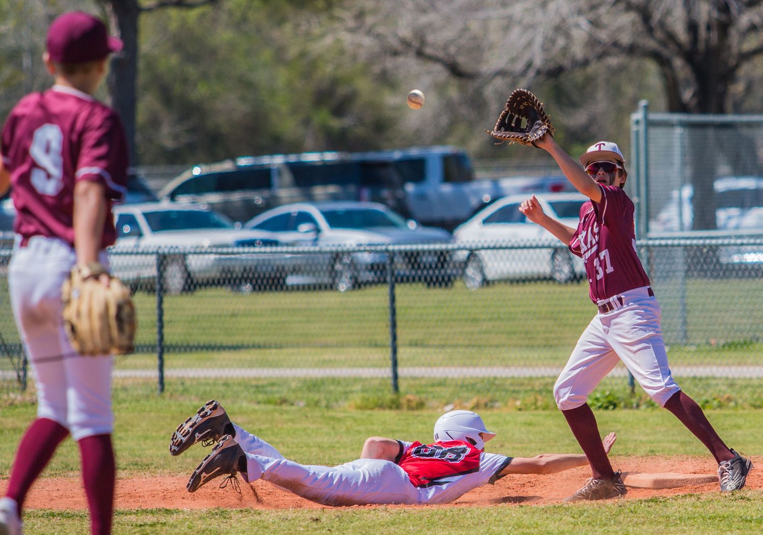 Baseball players in maroon uniforms practicing fielding drills on sunny day.