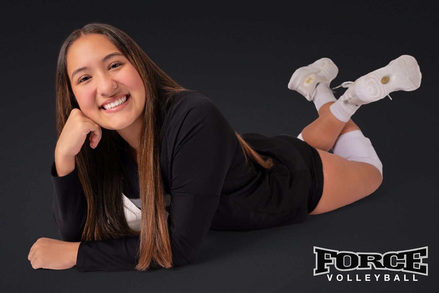 Volleyball player poses with ball in stylish black outfit against dark background for team photos.