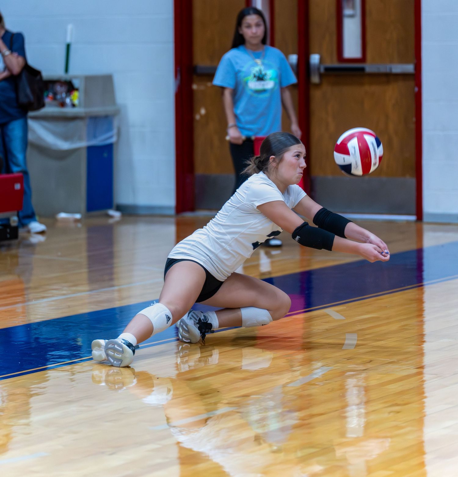 Player dives for volleyball during defensive play on indoor court.
