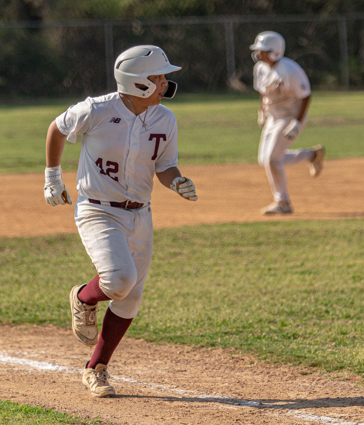 Baseball player in white uniform runs along baseline during game action.