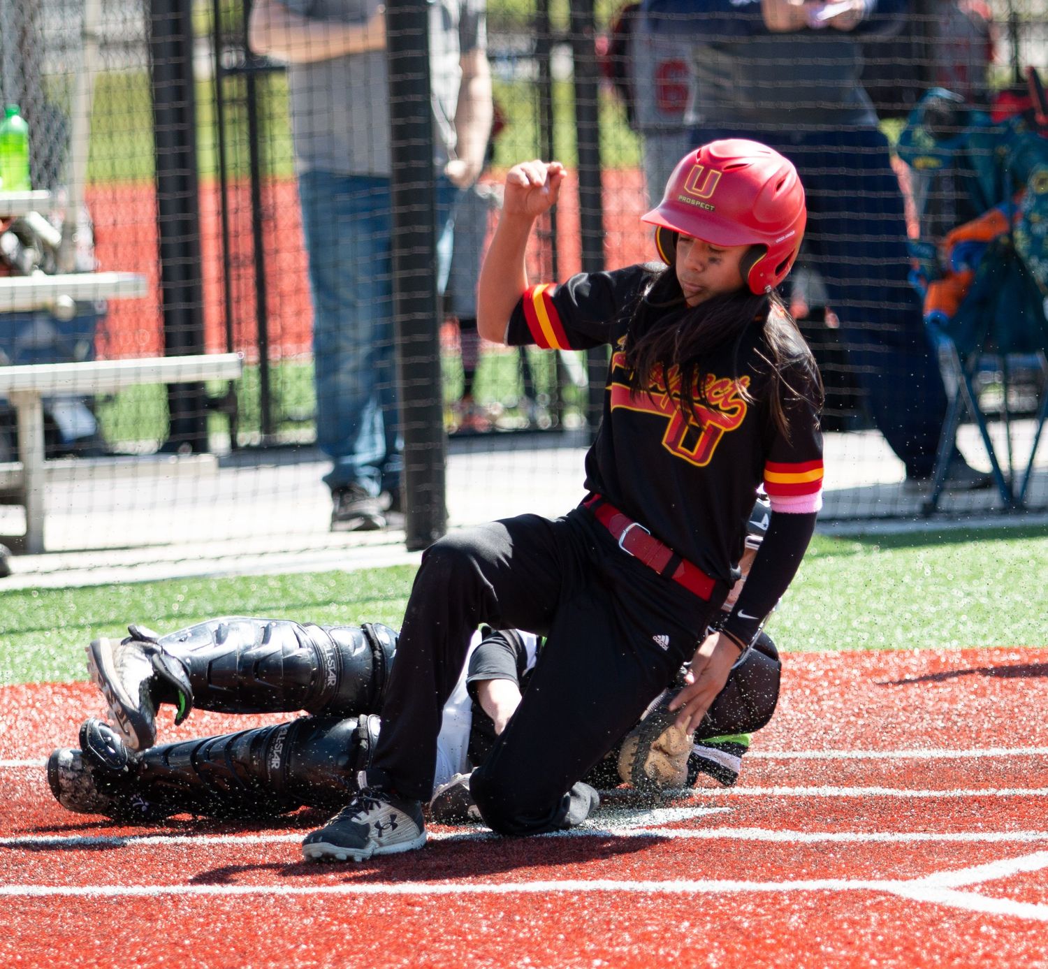 Baseball player in black uniform and red helmet slides into base during game.